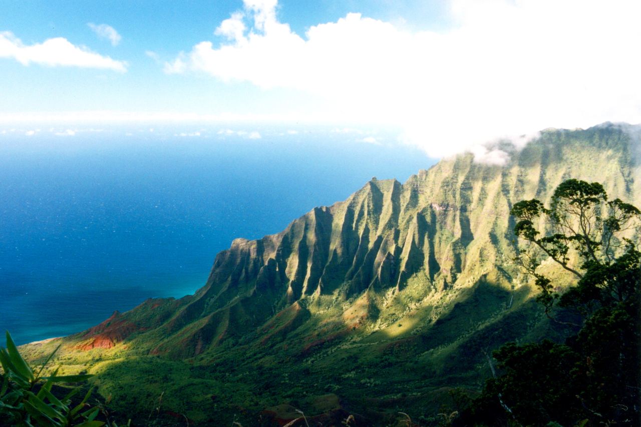Nā Pali-kustens gröna, veckade bergskammar som stupar ner mot det blå Stilla havet, sedda från en utsiktsplats ovanför Kalalaudalen på Kauaʻi