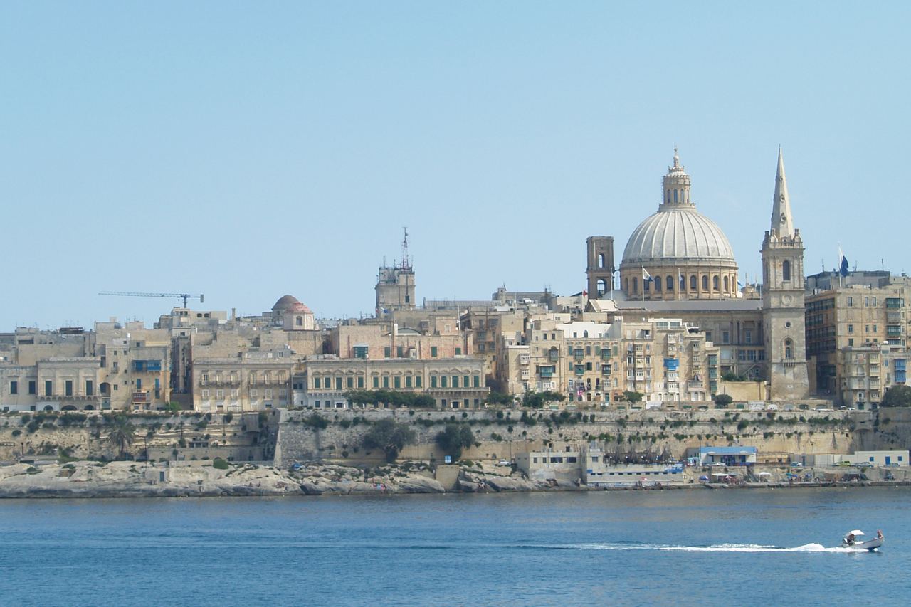 Vallettas siluett sedd från Sliema över vattnet, med den stora kupolen på Karmelitkyrkan och spiran på St Paul's Pro-Cathedral mot blå himmel